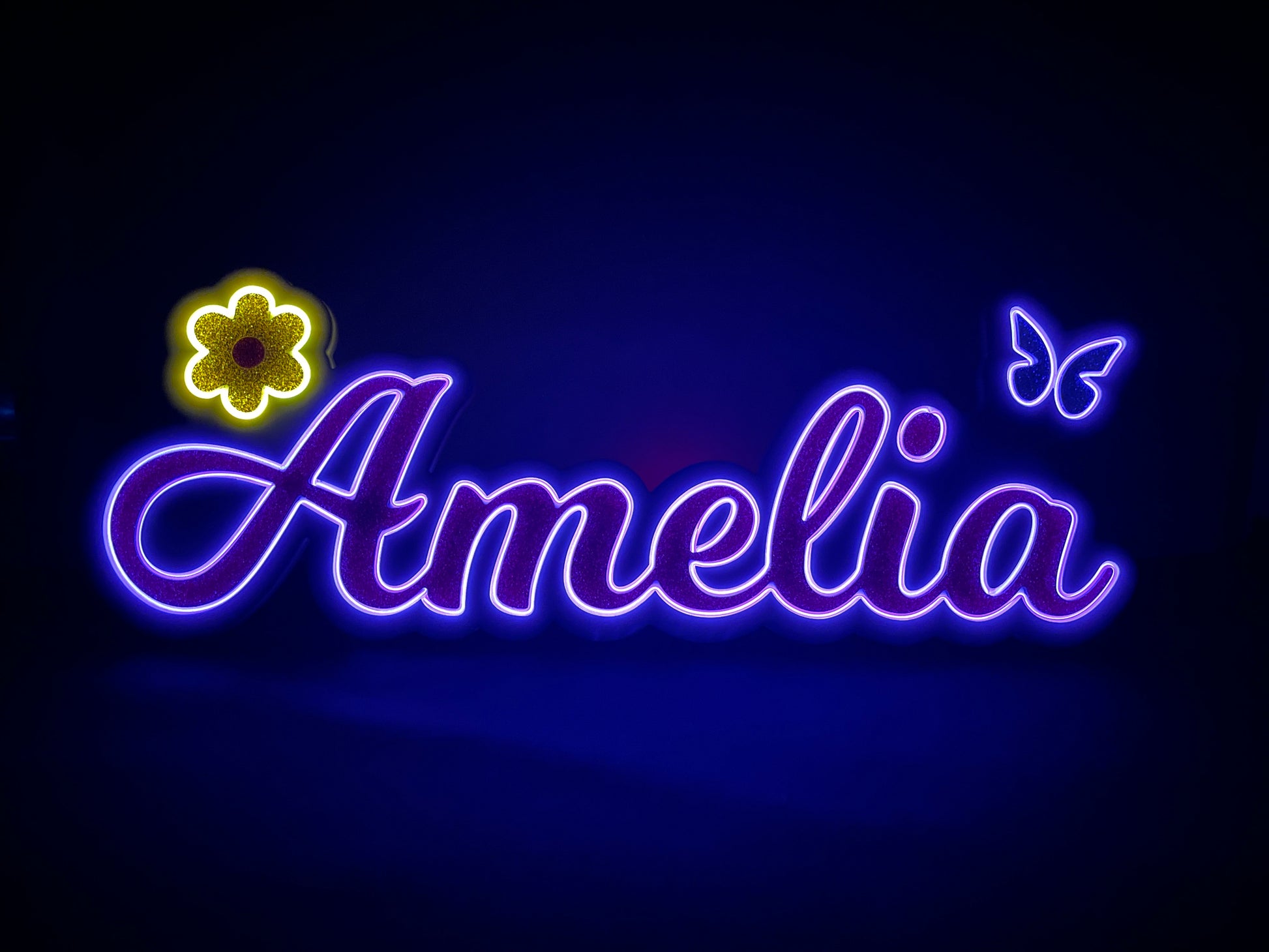 Amelia neon name light in purple with a gold flower at the beginning and a purple butterfly at the end displayed lit up