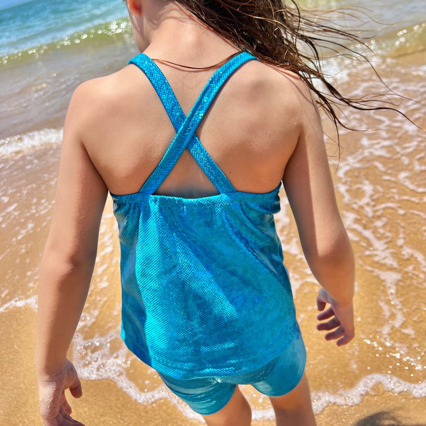 Back view of a Girl wearing a aqua blue singlet top and shorts gymnastic outfit playing on the beach