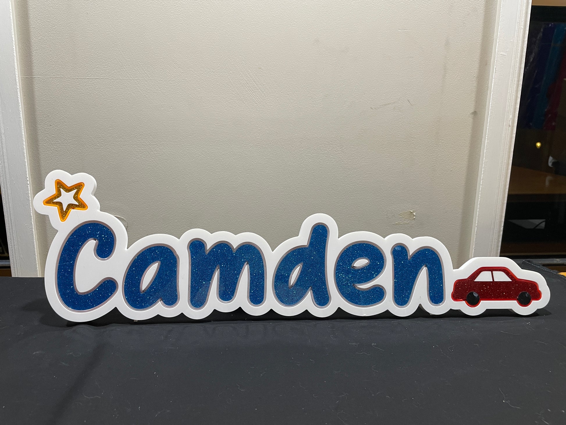 Camden neon name light in blue with a Star at the beginning and a red car at the end displayed during the day