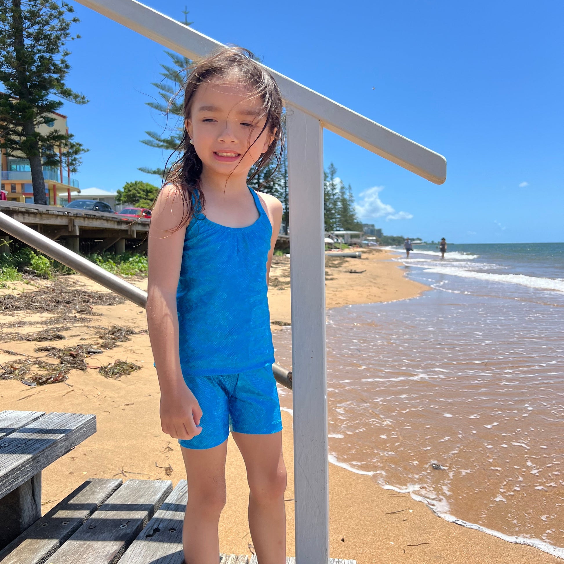 Girl wearing a aqua blue singlet top and shorts gymnastic outfit standing on stairs near the beach
