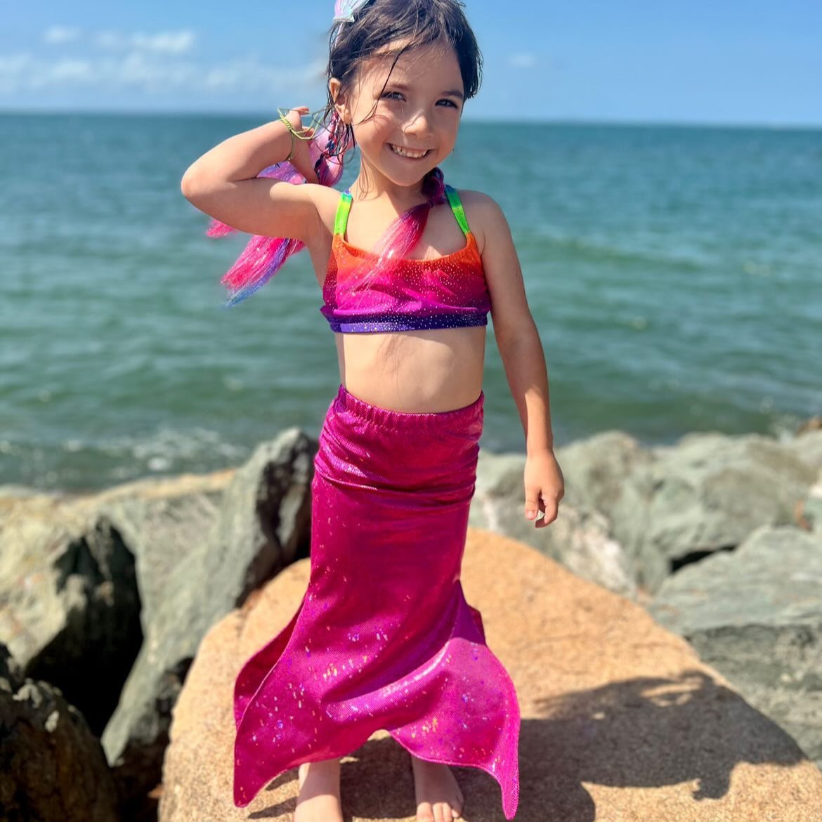 Girl wearing a bright rainbow crop top and hot pink walkable mermaid tail dress-up costume and the beach Brisbane Australia