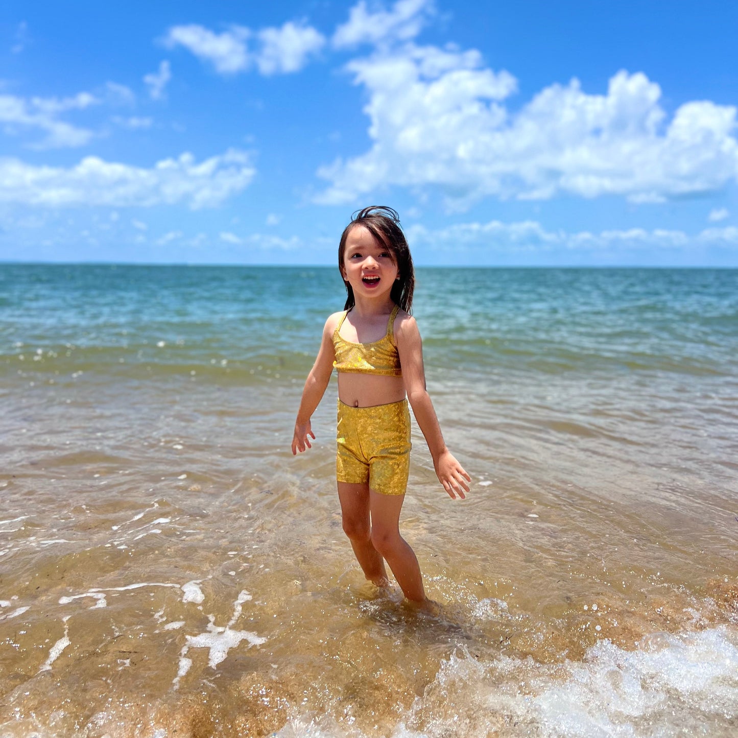 Girl wearing a gold crop top and gold shorts gymnastic outfit playing in the water at a beach