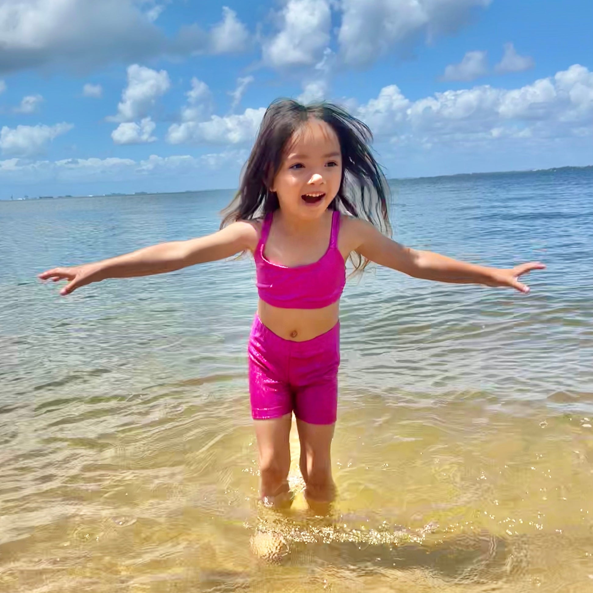 Girl wearing a hot pink crop top and shorts gymnastic outfit playing in the water at a beach