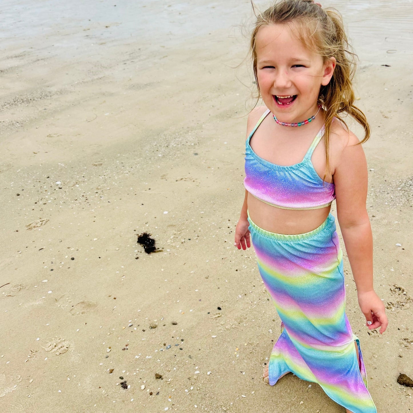 Girl wearing a pastel rainbow crop top and matching walkable mermaid tail dress-up costume standing a a beach Brisbane Australia