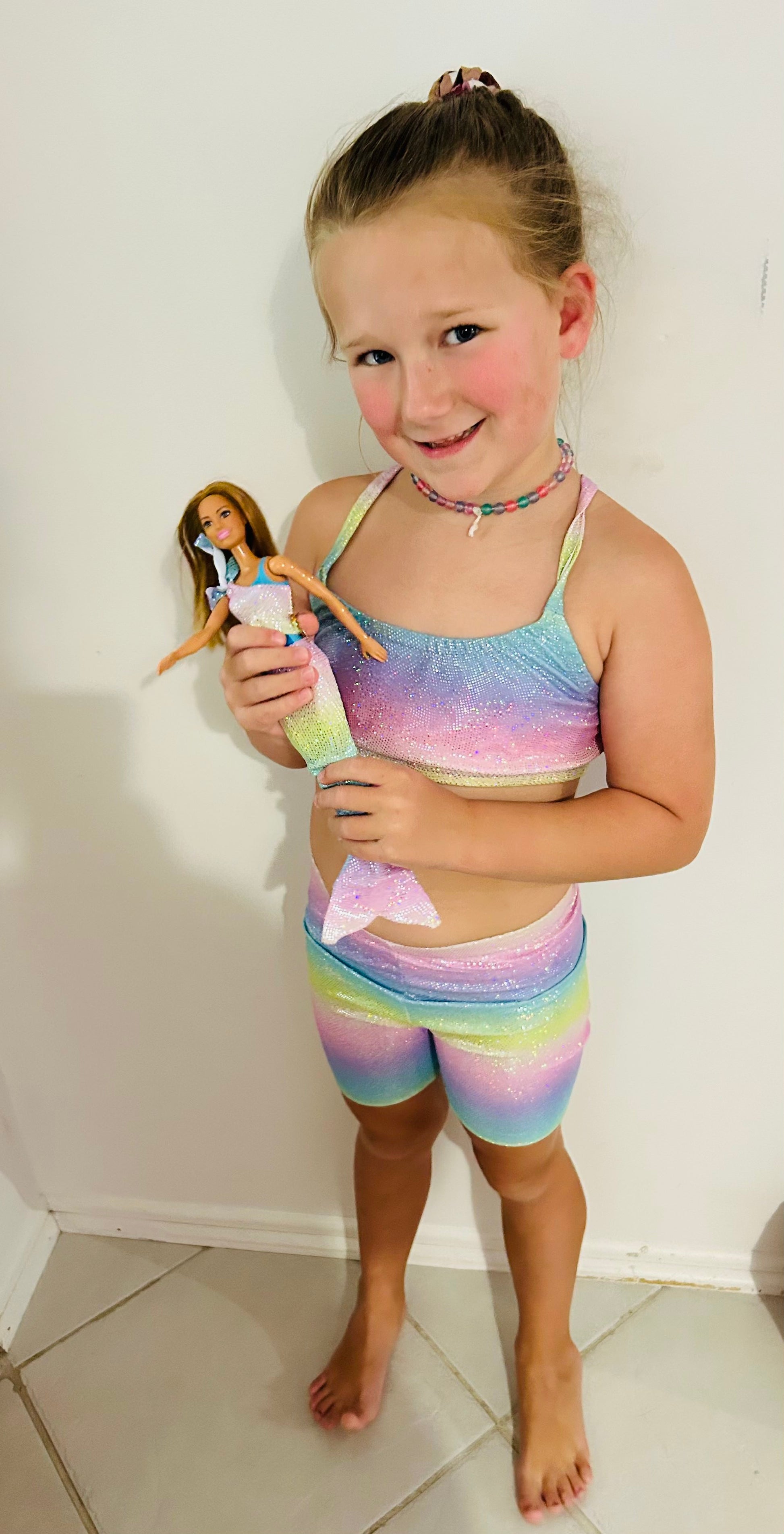 Girl wearing pastel rainbow crop top and matching shorts gymnastic outfit holding a doll Brisbane Australia