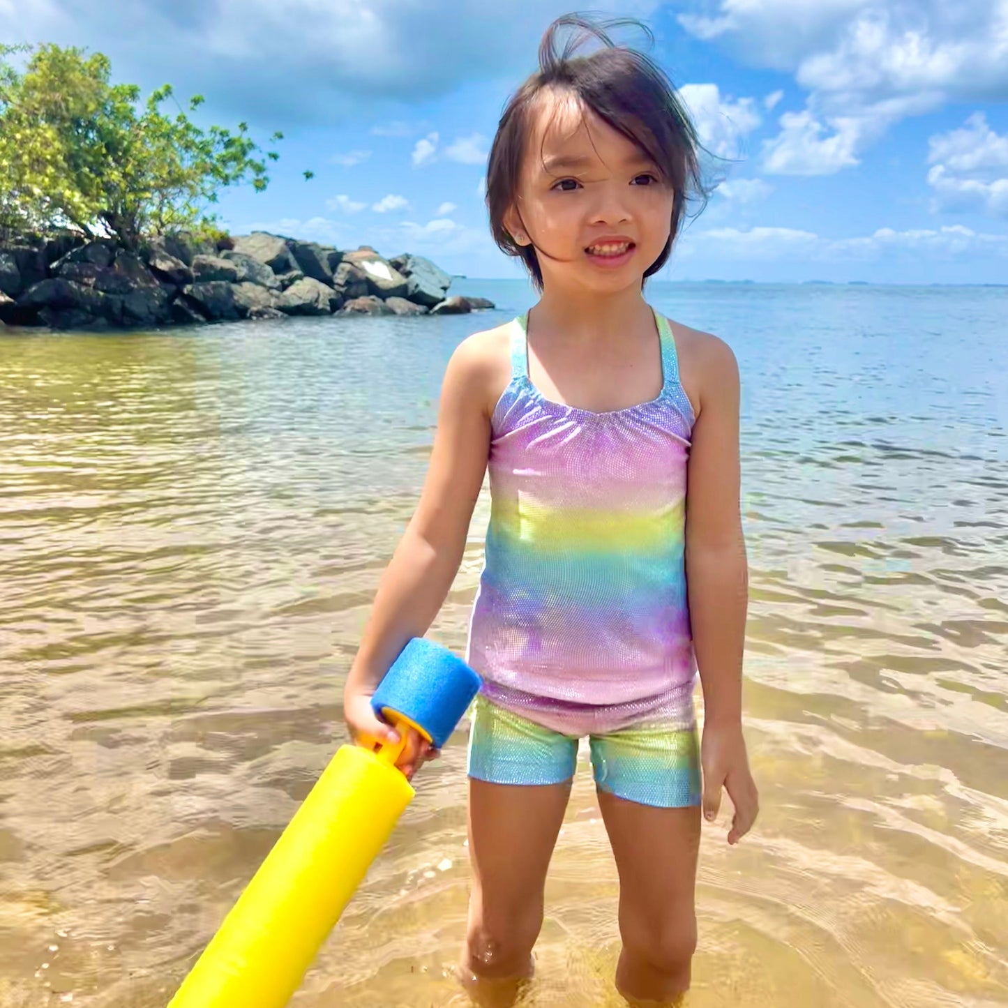 Girl wearing pastel rainbow singlet top and shorts gymnastic outfit playing in the water at a beach