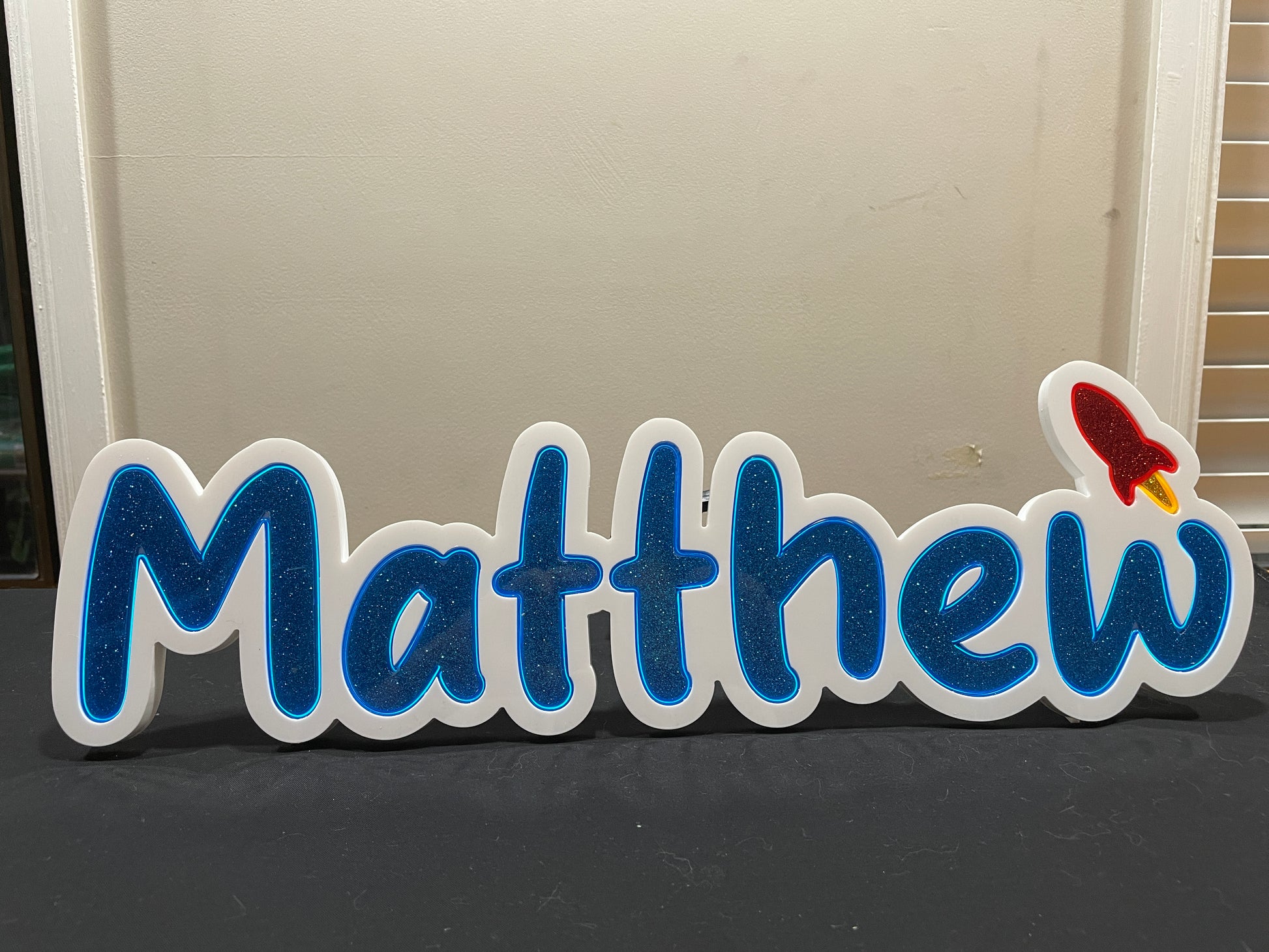 Matthew neon name light in blue and with a red rocket at the end not lit up