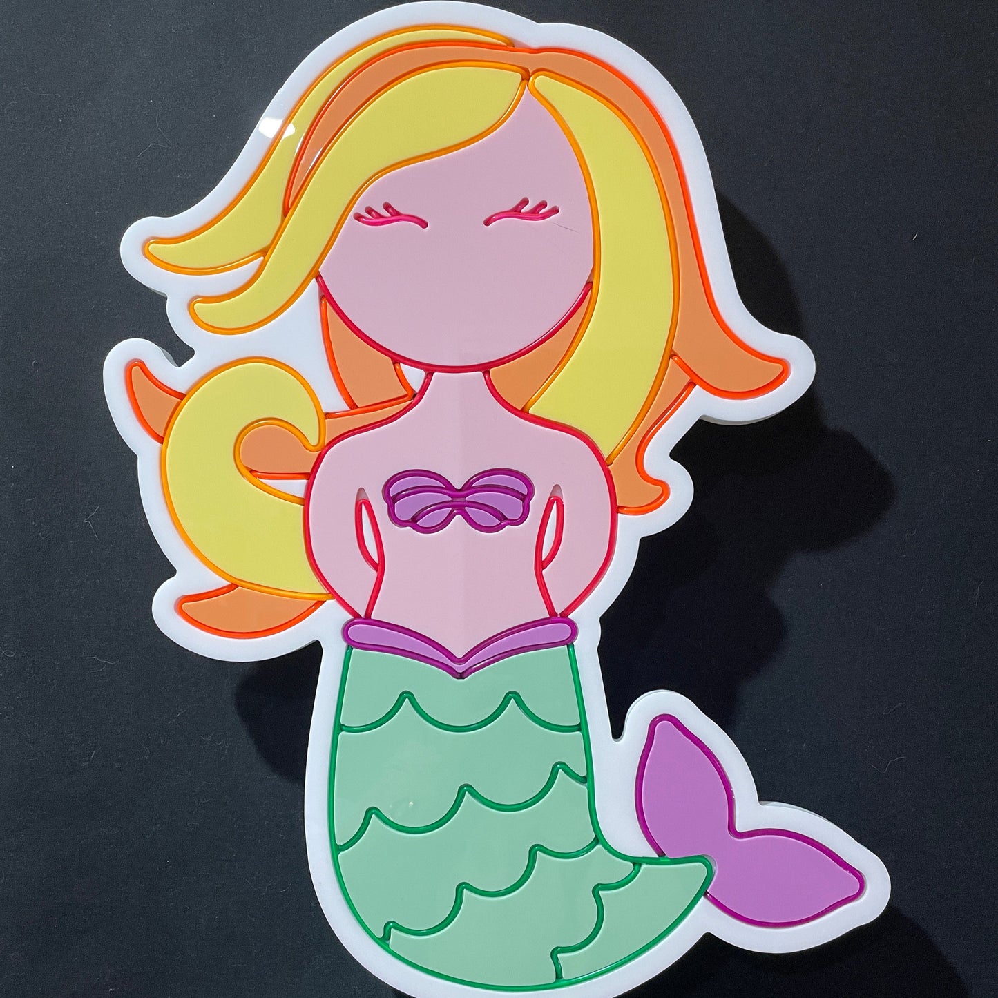 A neon light in the shape of a mermaid with a green tail and purple top not lit up