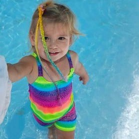 Toddler in a pool wearing bright rainbow singlet top and shorts Brisbane Australia
